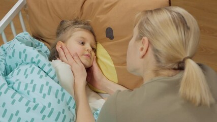 a mother examines the throat of her little daughter lying on the bed.