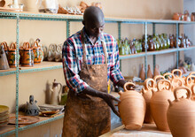 Concentrated African Craftsman Examining Handmade Earthenware During Work In Pottery Workshop