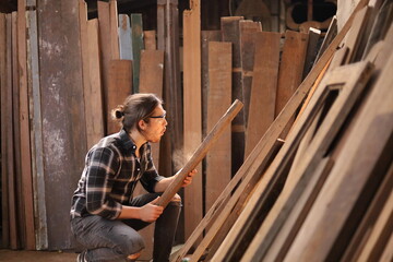 Wall Mural - Young Caucasian carpenter man is blowing sawdust from plank of wood in his own garage style workshop for hobby with copy space