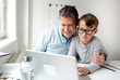 © epiximages - Father and son sitting in front of the laptop, working from home with help from his son.