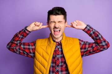 Poster - Photo of upset angry young man wear yellow sleeveless jacket fingers ears not want hear isolated violet color background