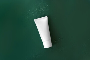 Top view mockup facial skincare white tube product bottle with blank label on Tidewater Green solid color plain background with droplets