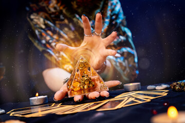 Poster - The fortune teller holds a glass pyramid with gold in her hands and casts a spell over it. Magic aura. There are Tarot cards on the table. Close-up. The concept of divination, magic and esotericism