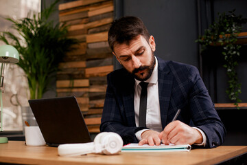 Young businessman using laptop in his office. Businessman taking a notes while working on laptop.