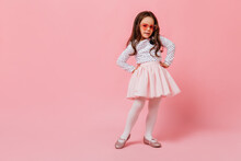 Charming Girl In Fluffy Skirt Posing On Pink Background. Curly Baby Wearing Heart-shaped Glasses