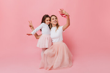 Wall Mural - Woman in white T-shirt and pink skirt makes selfie with little girl in same outfit