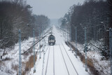 Fototapeta  - Dwutorowy szlak kolejowy zimą z przejeżdżającą lokomotywą elektryczną.