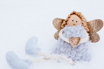 A soft textile doll with golden heart in hands sitting on the snow. Valentine’s Day, love, Merry Christmas, New Year concept.