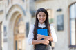 © be free - Happy small kid with school look wear uniform holding library book outdoors, knowledge