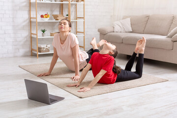 Covid lockdown sports. Teen girl and her mother doing yoga flexibility poses to video tutorial course at home