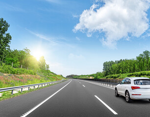 A white car rushes along the road against the backdrop of a beautiful countryside landscape.