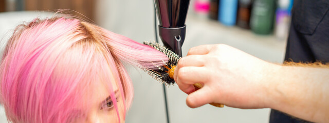 Hairdresser dries pink hair of the young woman in a beauty salon