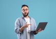 © Prostock-studio - Surprised millennial guy opening mouth in awe, pointing at laptop screen with shocking web content on blue background