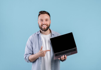 Poster - Positive young man pointing at empty laptop screen with space for your website design over blue background, mockup