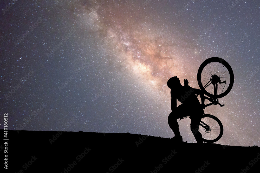 Cyclists carry mountaineering up the mountain with a starry background and the Milky Way. - obrazy, fototapety, plakaty 
