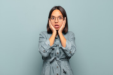 Wall Mural - young hispanic woman feeling horrified and shocked, raising hands to head and panicking at a mistake