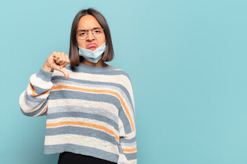 Wall Mural - young hispanic woman feeling cross, angry, annoyed, disappointed or displeased, showing thumbs down with a serious look