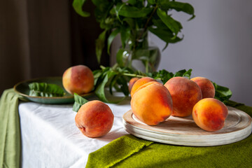 Peaches on table in kitchen near window. Rustic minimalism food peach fruits with leaves on wooden board on tablecloth. Harvest of Ripe juicy peaches. Still life Peaches fruit