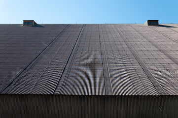 Construction building roof pattern with blue sky. Ribbed roof of warehouse of cargo terminal in dry cargo port. Industrial building rooftop. Grunge texture. Industrial background and copy space