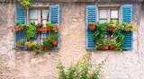 Fototapeta Krajobraz - Vintage, traditional italian house wall with old blue window shutters and many plant pots. Typical european postcard view.