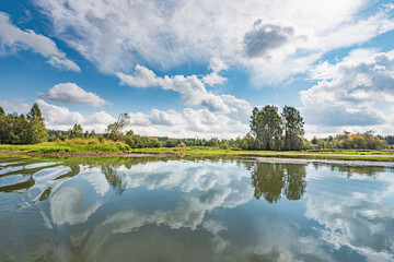 Wall Mural - panoramic landscape on a sunny day on the river with the sky in the clouds and the reflection in the
