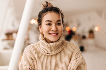 lady in stylish beige oversize sweater looks into camera. shot of girl with bun in massive earrings 