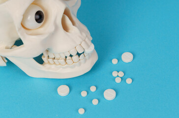 On a blue background, a skull that holds pills in its mouth. Pills are scattered nearby