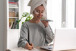 © DimaBerlin - Busy woman with towel on head and patches under eyes, working from home on laptop during lockdown, records a voice message on smart phone, makes notes. Face skin care beauty. Real life.