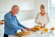 © Angela Waterton/Westend61 - Senior couple cutting food on kitchen island at home