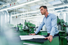 Male Professional With Floor Plan Looking Away While Working In Factory