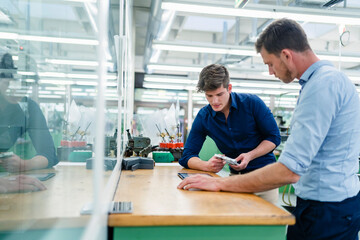 Male engineer holding machine part having meeting with colleague on desk in industry