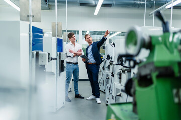 Male professional pointing at machinery equipment while discussing in industry