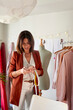 © Veam/Westend61 - Female fashion entrepreneur using smart phone standing by clothes rack in design studio