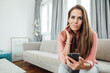 © Joseffson/Westend61 - Mature woman with hand in hair holding mobile phone in living room at home