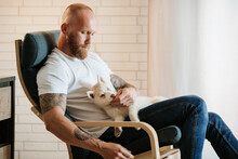 Man Sitting With Siberian Husky Puppy On Armchair At Home
