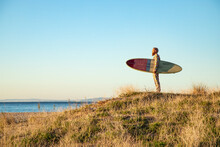 Man Looking At Sea View While Standing With Surfboard On Beach