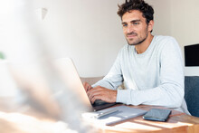 Mid Adult Man Working On Laptop While Sitting By Table At Home