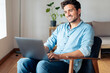 © steve brookland/Westend61 - Smiling man using laptop while sitting on armchair at home