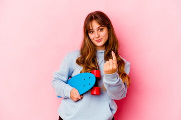 Wall Mural - Young skater woman isolated on pink background pointing with finger at you as if inviting come closer.