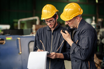 Two workers at an industrial. technician engineer checking process on notebook to machinery in factory. workers using machine equipment in factory