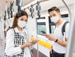 © Bangkok Click Studio - Portrait of young adult Asian couple with a medical mask standing and holding a smartphone while looking camera with blurred Skytrain background during covid-19 pandemic. New normal lifestyle concept