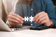 © NINENII - Business partnership concept. Businessman hand connecting jigsaw puzzle with calculator at office in morning light.