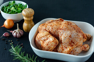 Whole raw chicken with herbs and spices ingredients on dark background ready to cook