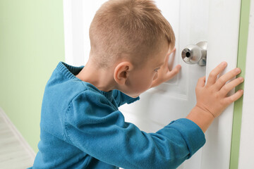 Cute little boy looking through keyhole in closed door