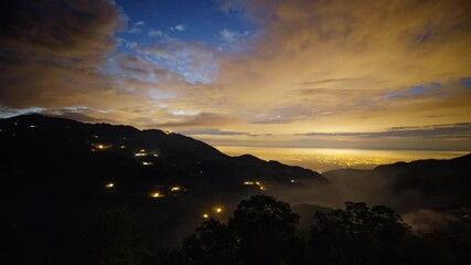 Wall Mural - Time lapse of a mountain landscape in Taiwan as twilight turns to night and the stars appear. Lights of a town can be seen in the distance.