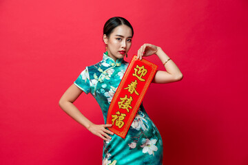 Wall Mural - Asian woman wearing oriental cheongsam dress presenting Chinese new year label in red isolated studio background, text means wishing of prosperity