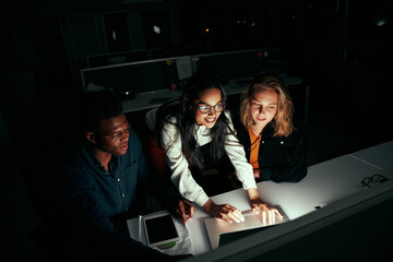 Successful multiethnic business team working on laptop over office desk at night