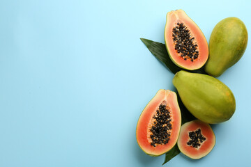 Sticker - Fresh ripe papaya fruits with green leaves on light blue background, flat lay. Space for text