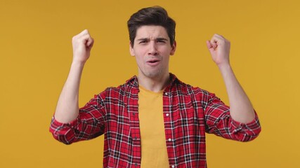 Wall Mural - Shocked surprised young man 20s years old in casual red checkered shirt posing isolated on yellow background in studio. People lifestyle concept. Say wow screaming spreading hands doing winner gesture