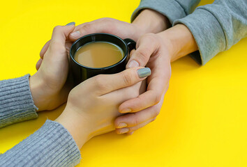 Wall Mural - Hands on a yellow background with coffee, love. Coffee with milk, black cup. Selective focus.